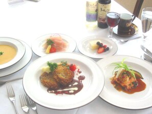 A table set with various dishes, including a soup, a salad, and a meat dish, along with two bottles of wine and a glass of water. - Pension Ing Tomamu (Shimukappu)