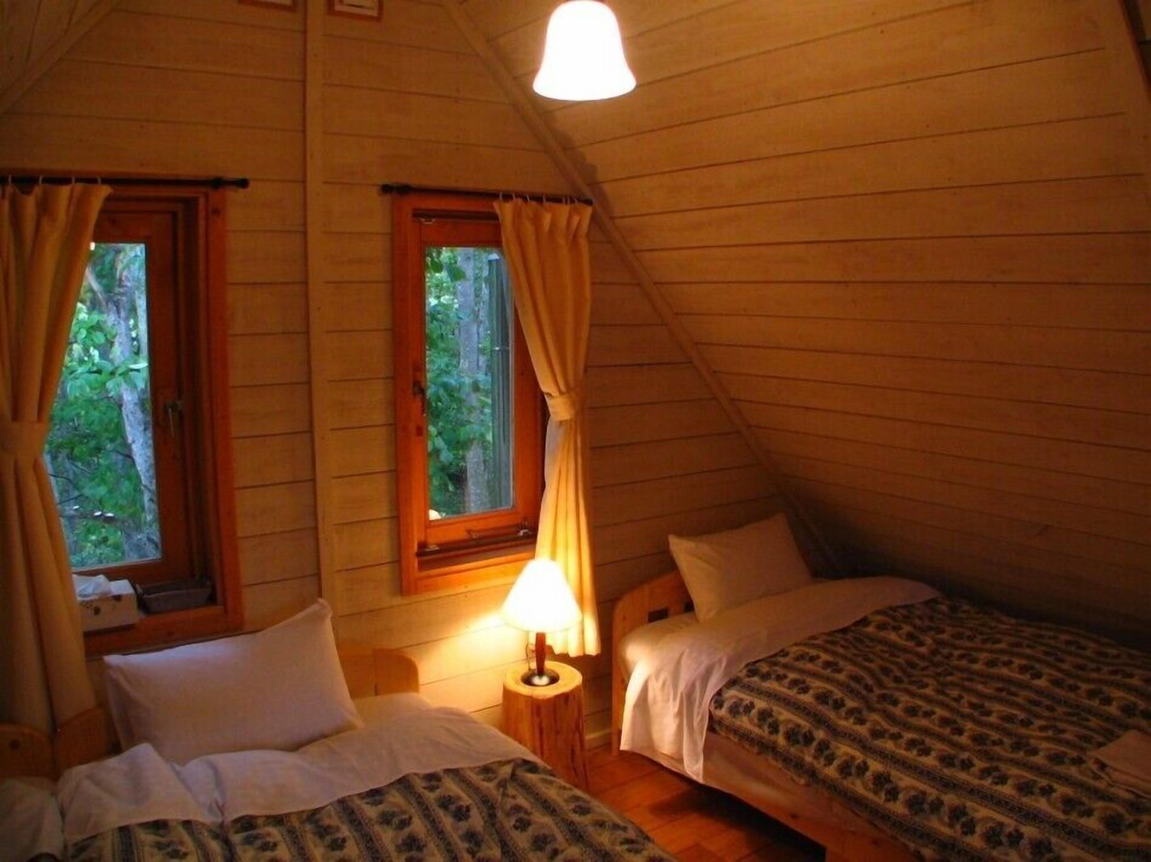 Een knus zolderkamer met twee bedden, houten wanden en een raam met gordijnen.