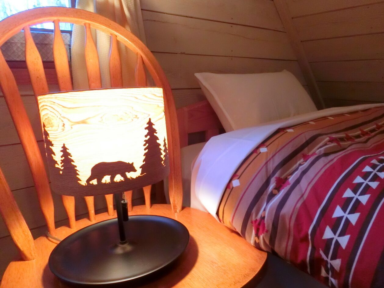 Une chaise en bois dotée d’une lampe à rétroéclairage représentant la silhouette d’un ours et d’arbres, un lit avec une couverture à motifs et un oreiller blanc.