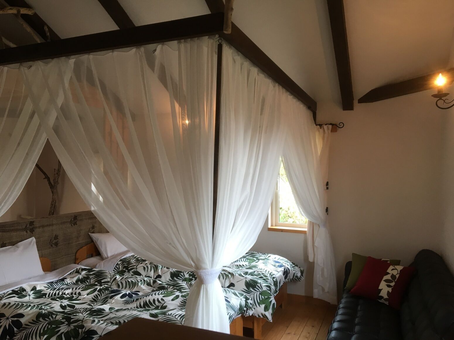 Une pièce avec un lit sous un dais, une fenêtre, un canapé et un plafond en bois.