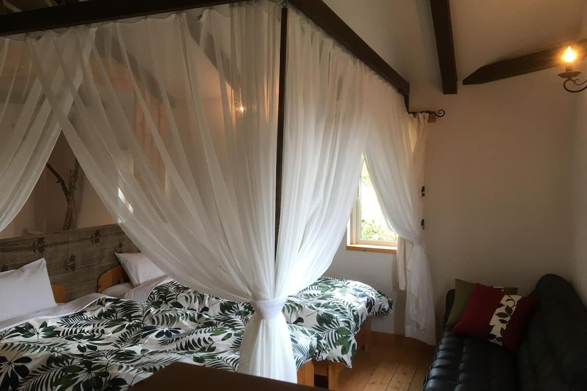 Una habitación con una cama bajo un dosel, una ventana, un sofá y techo de madera.