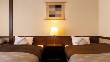 A hotel room with two beds, a nightstand with a lamp, and a small wall-mounted artwork.