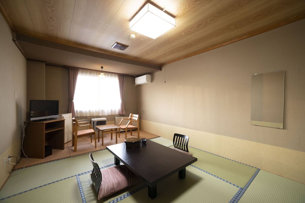Ett traditionellt japanskt rum med tatamimattor på golvet, ett lågt bord, stolar, en tv och en skjutdörr.