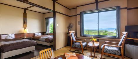 A hotel room with a bed, two chairs, a small table, and a large window offering a view of the outdoors.