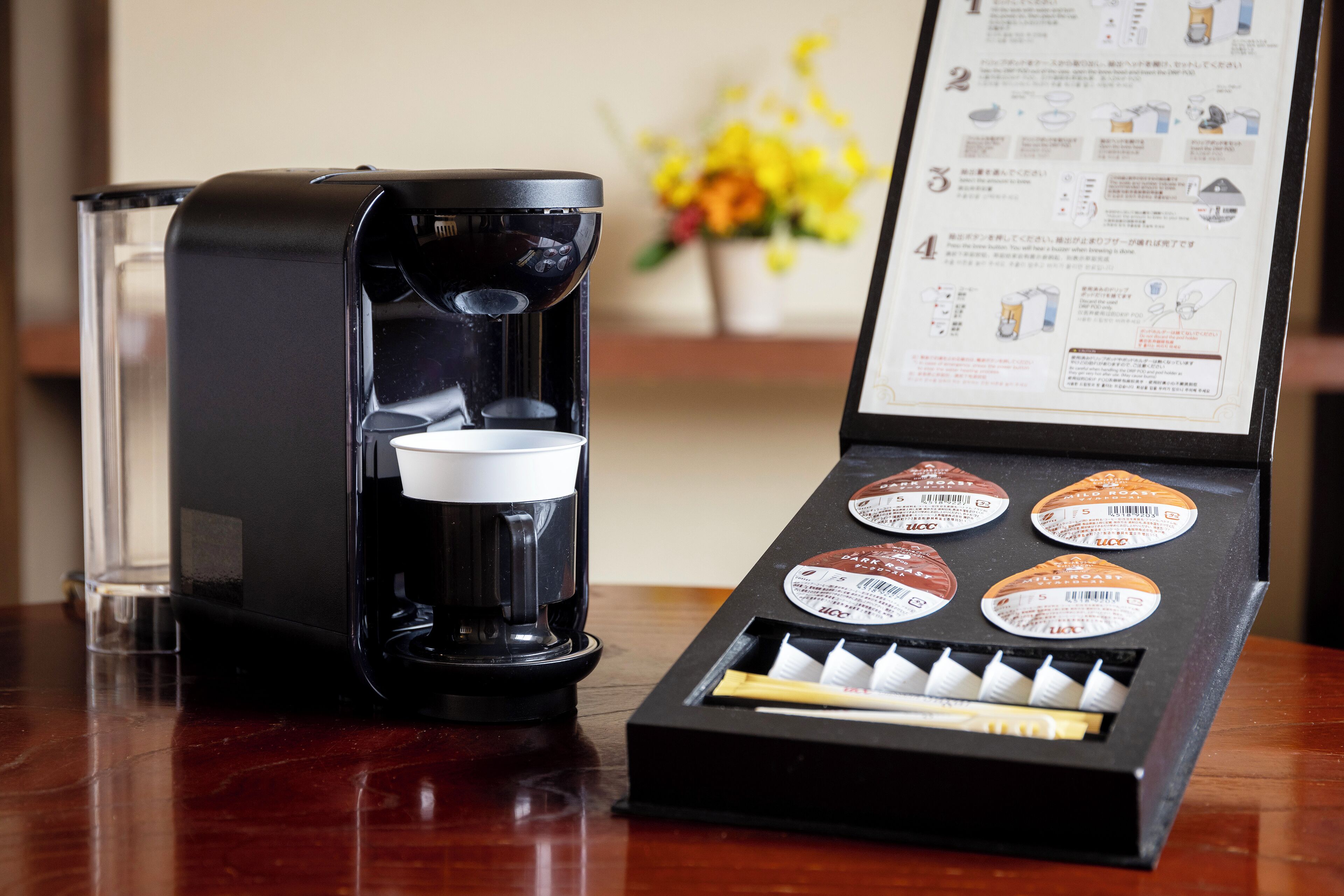 A coffee maker with a cup and a box of coffee pods on a wooden table.