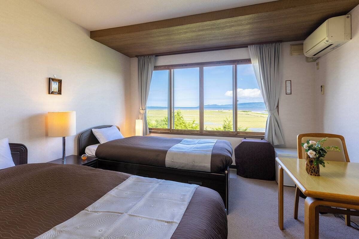 Ett hotellrum med två sängar, ett skrivbord, en stol och ett stort fönster med utsikt över landskapet.