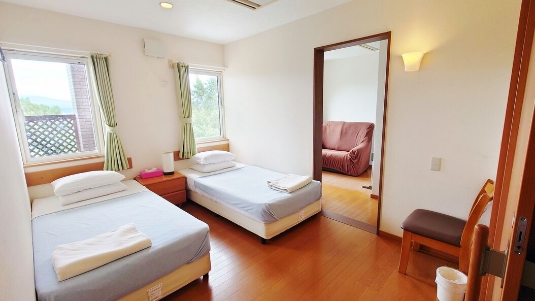 A bedroom with two beds, a wooden floor, a mirror, a chair, and a window with curtains.
