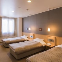 Habitación de hotel con tres camas, una mesita de noche con teléfono y una ventana con cortinas.