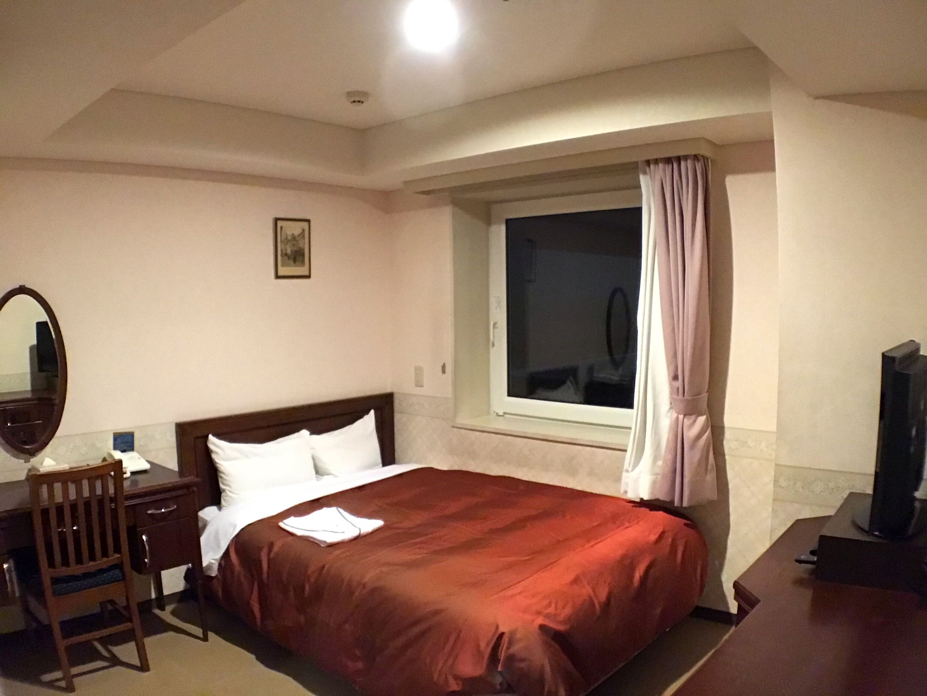 Een hotelkamer met een bed, een bureau, een stoel, een raam met gordijnen en een televisie.