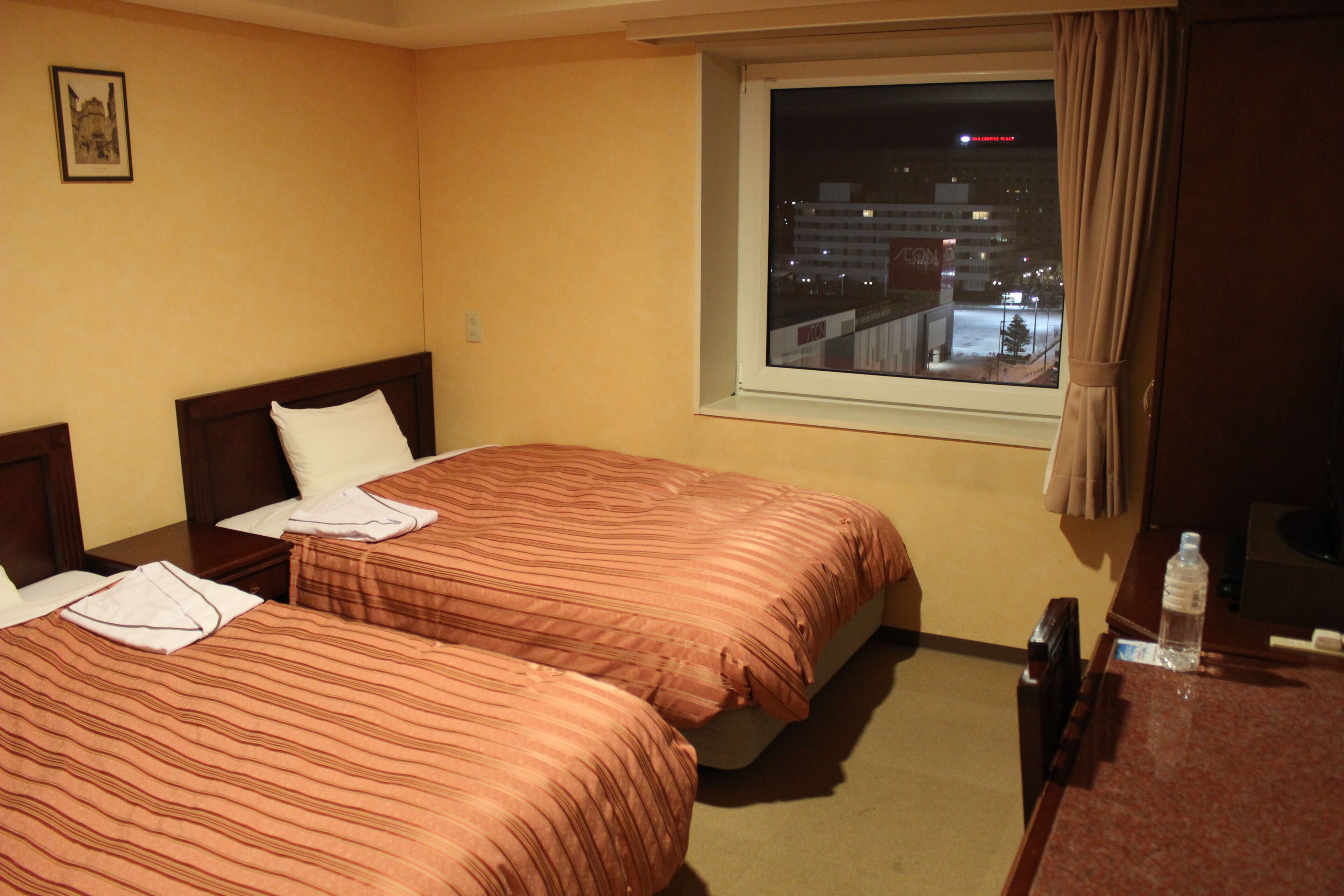 Een hotelkamer met twee bedden, een raam met uitzicht op de stad en een tafeltje met een fles.