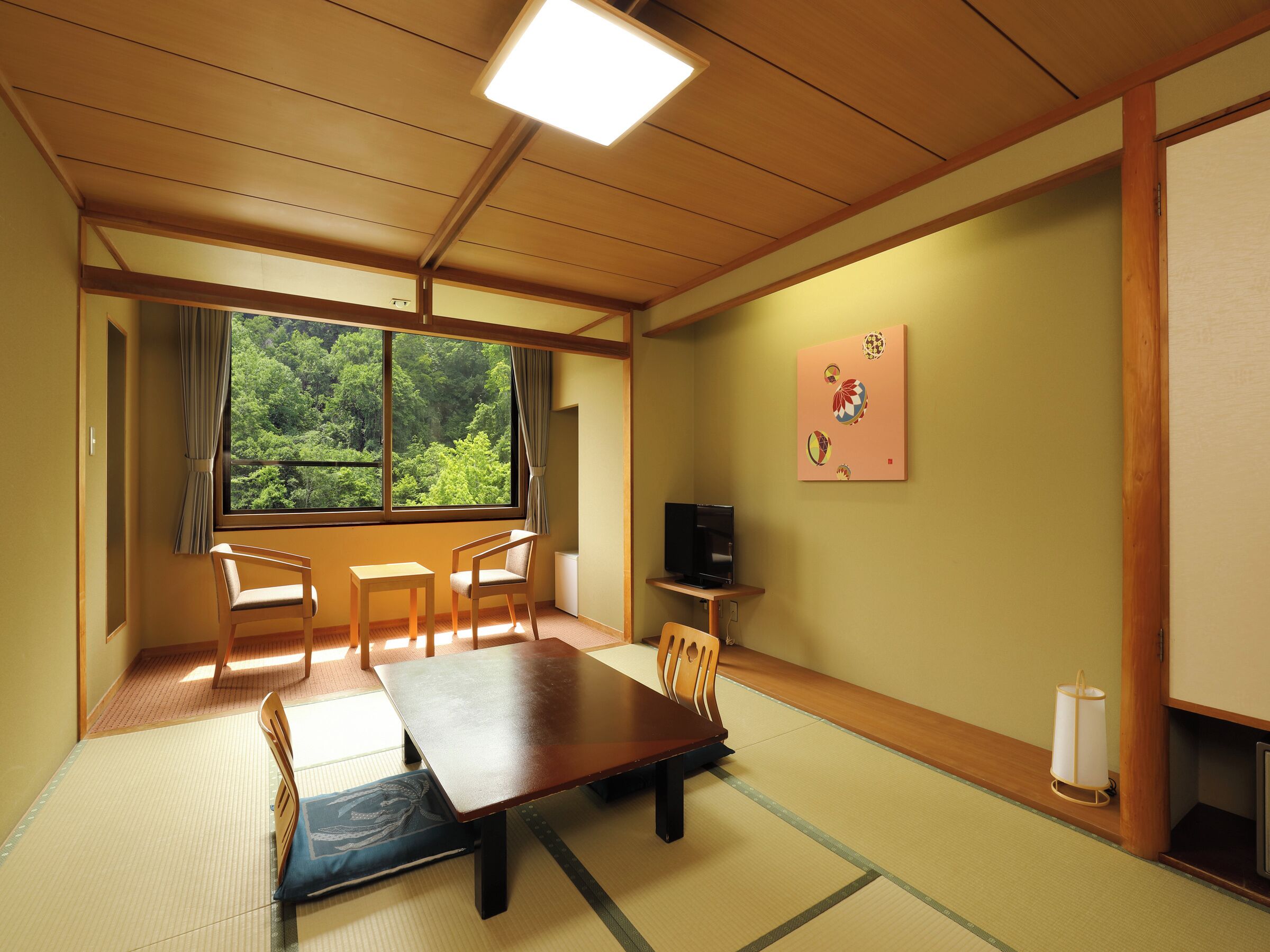 Una tradizionale stanza giapponese con pavimento in tatami, un tavolino, sedie, una televisione e una finestra con vista sugli alberi.