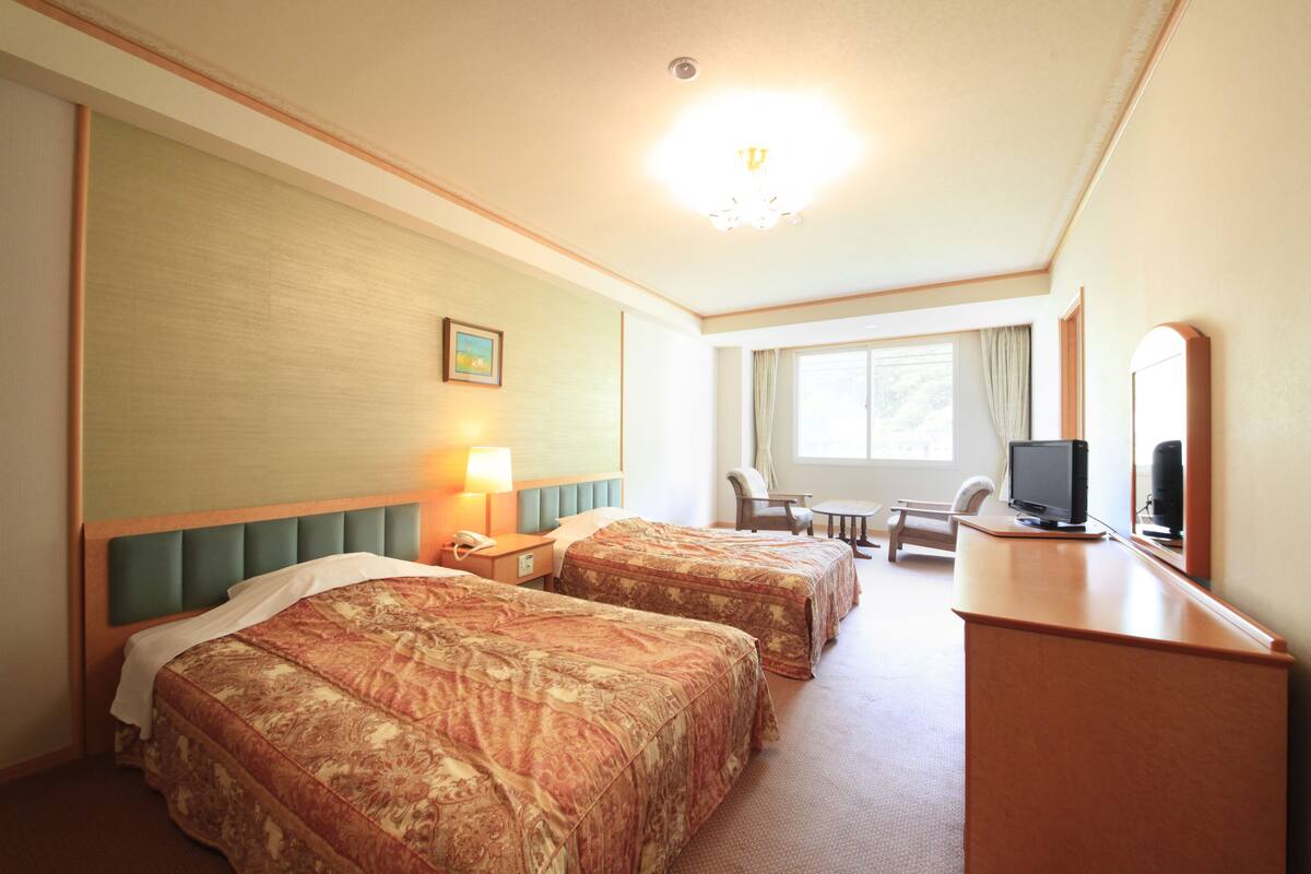 Ett hotellrum med två sängar, ett skrivbord med en tv, en stol och ett fönster med gardiner.