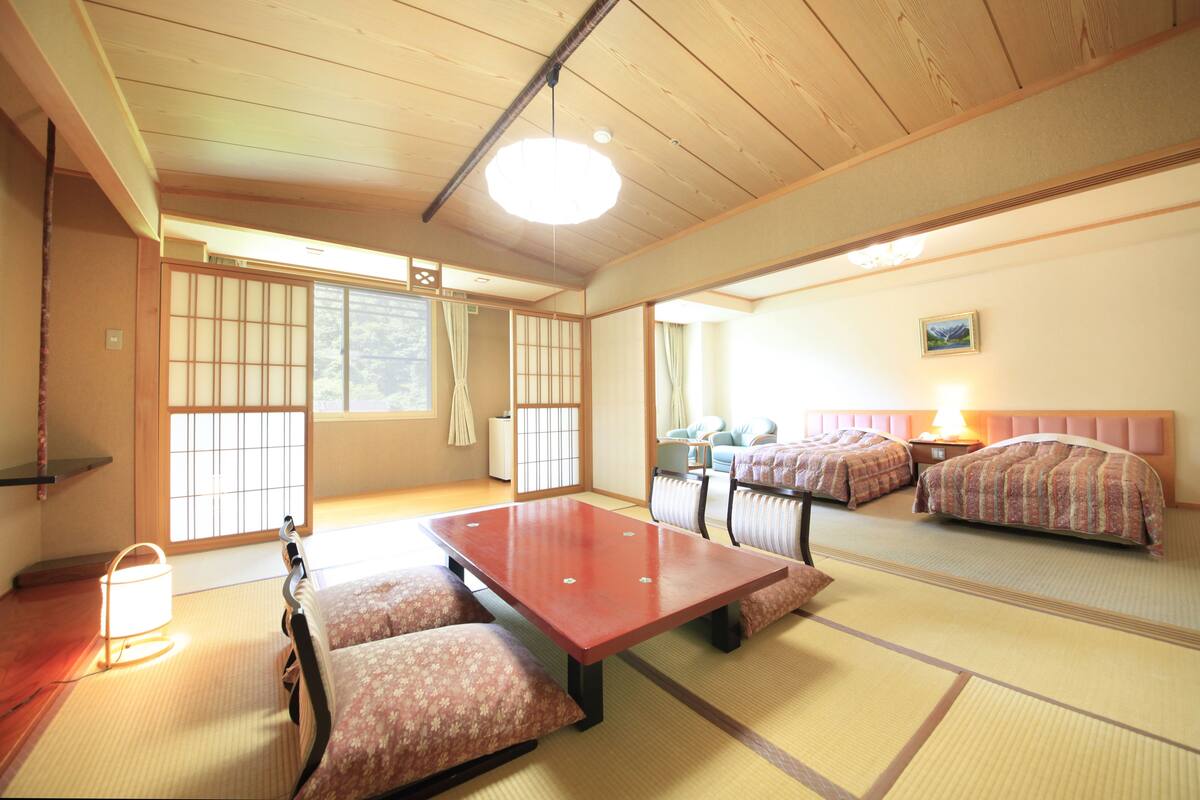 Ett traditionellt japanskt rum med tatamimattor på golvet, ett lågt träbord, två sängar med mönstrat sänglinne och skjutbara shojidörrar.