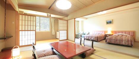 A traditional Japanese room with tatami flooring, a low wooden table, two beds with patterned bedding, and sliding shoji doors.