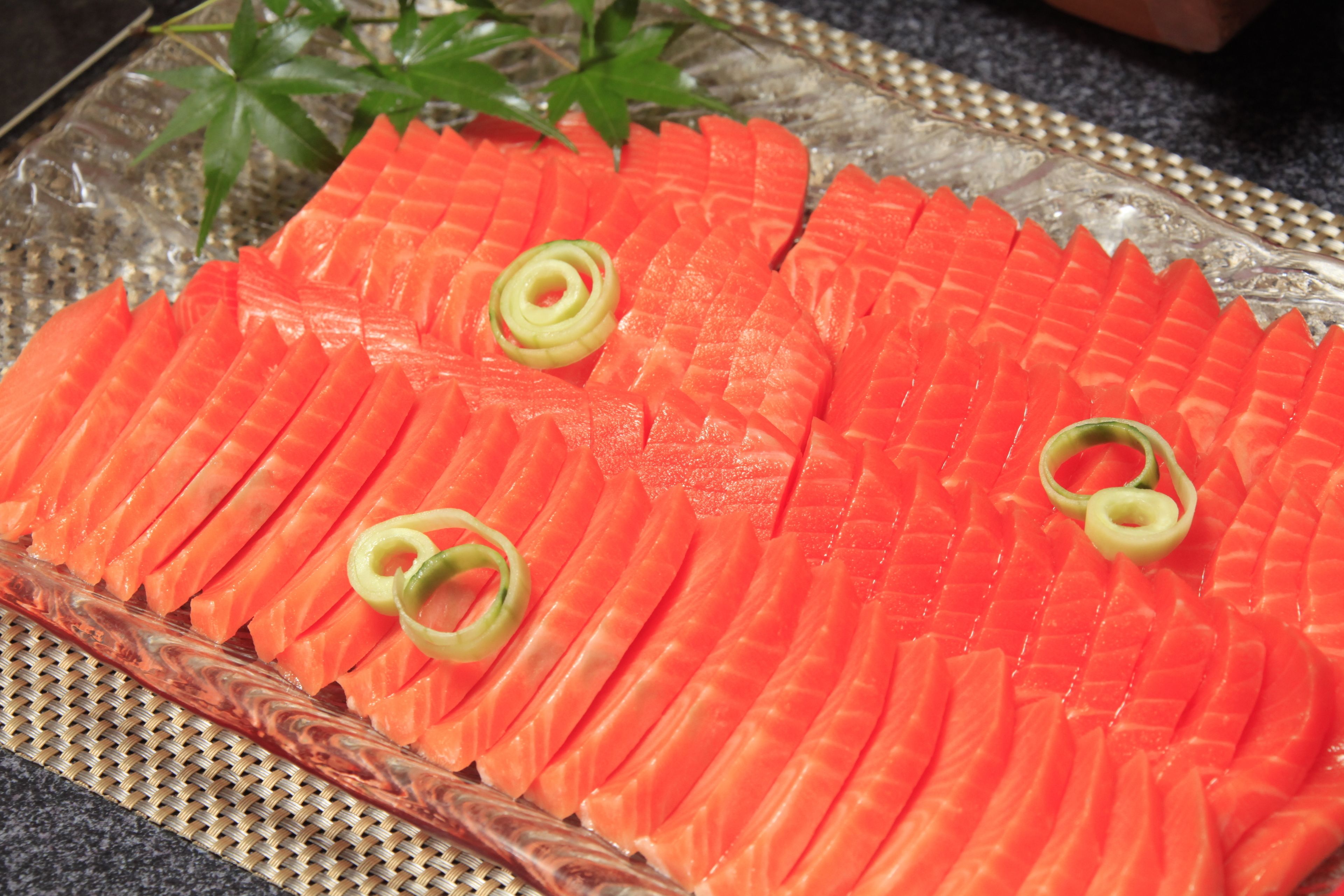 Un plato de vidrio con rebanadas de salmón ordenadas, adornadas con cebollines.