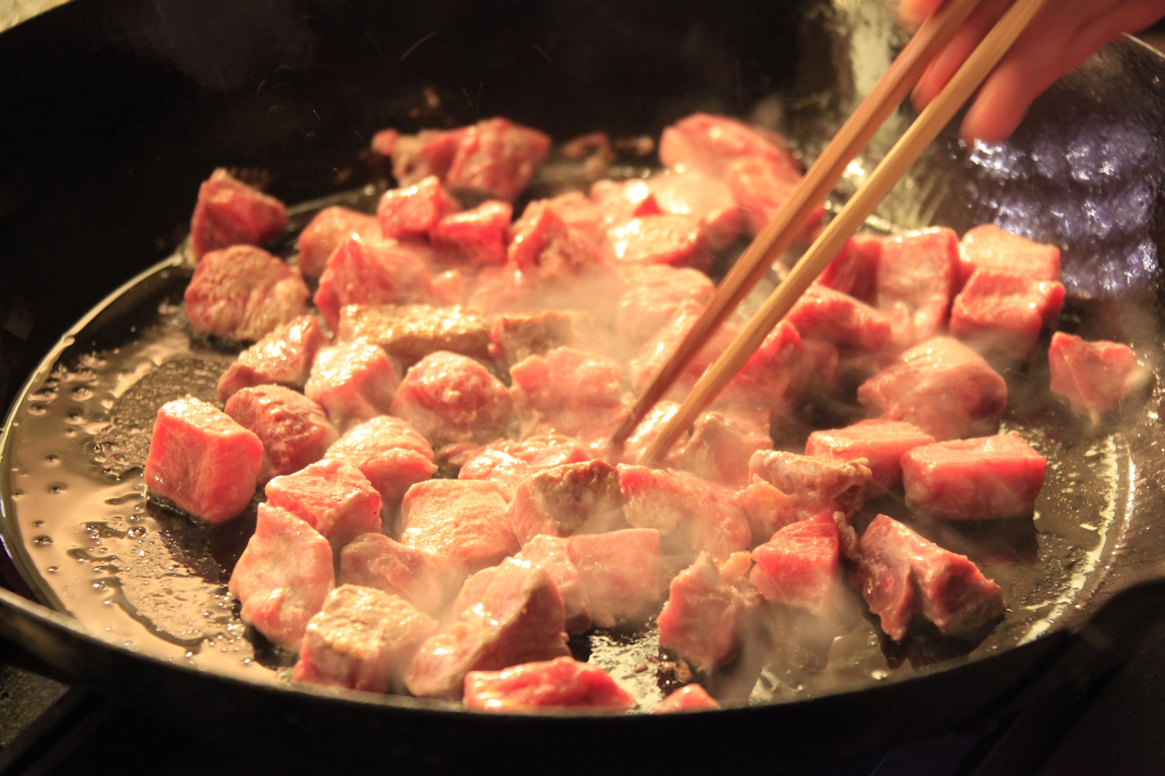 A close-up of meat being cooked in a pan.