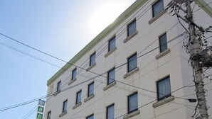 A multi-story building with a row of windows on each floor, a green awning, and a sign indicating a parking area.
