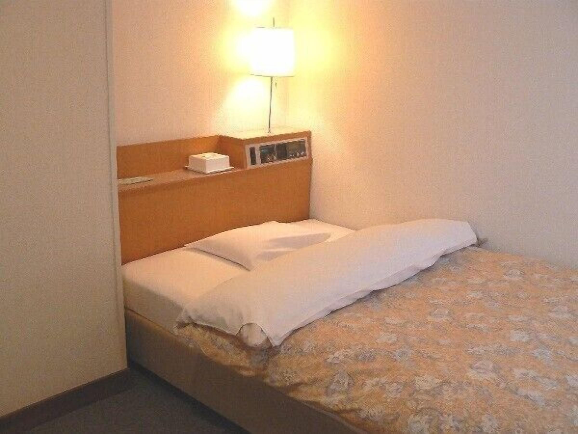 A single bed with a wooden headboard, a bedside table with a lamp, and a small box on the table.