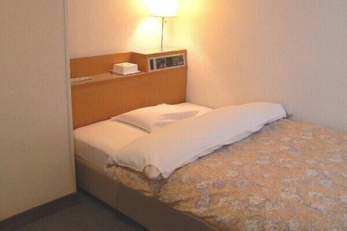 A single bed with a wooden headboard, a bedside table with a lamp, and a small box on the table.