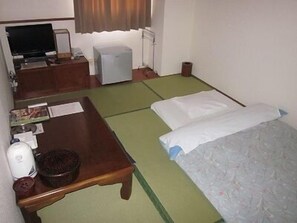 A hotel room with a bed, a desk, a television, and a small heater. - Kitaguchi Hotel (Kitami)