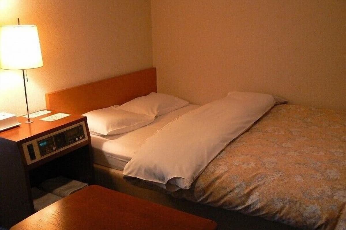 A hotel room with a bed, a bedside table with a lamp, and a small desk with a computer.