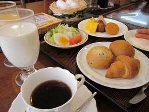 A breakfast table with plates of food, a basket of eggs, a glass of milk, and a cup of coffee. - Kitaguchi Hotel (Kitami)