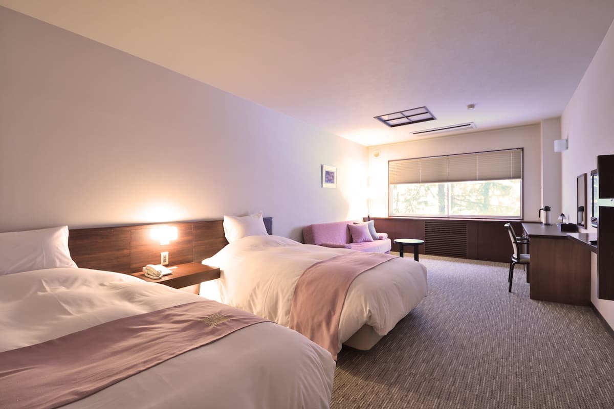 Ein Hotelzimmer mit zwei Betten, einem Schreibtisch, einem Stuhl, einem großen Fenster und einem Spiegel.