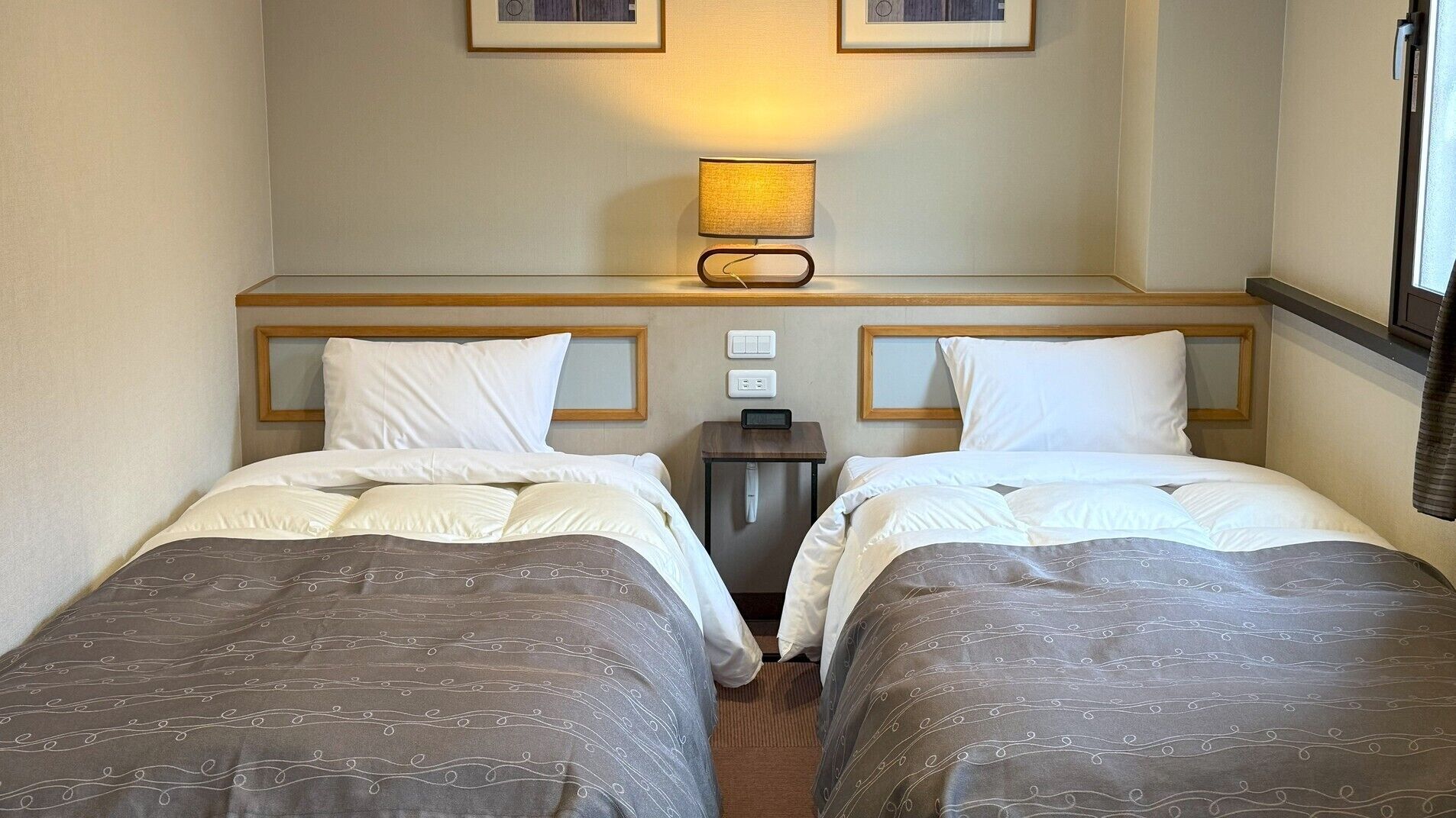Una habitación de hotel con dos camas, una mesita de noche con lámpara y un aplique de pared.