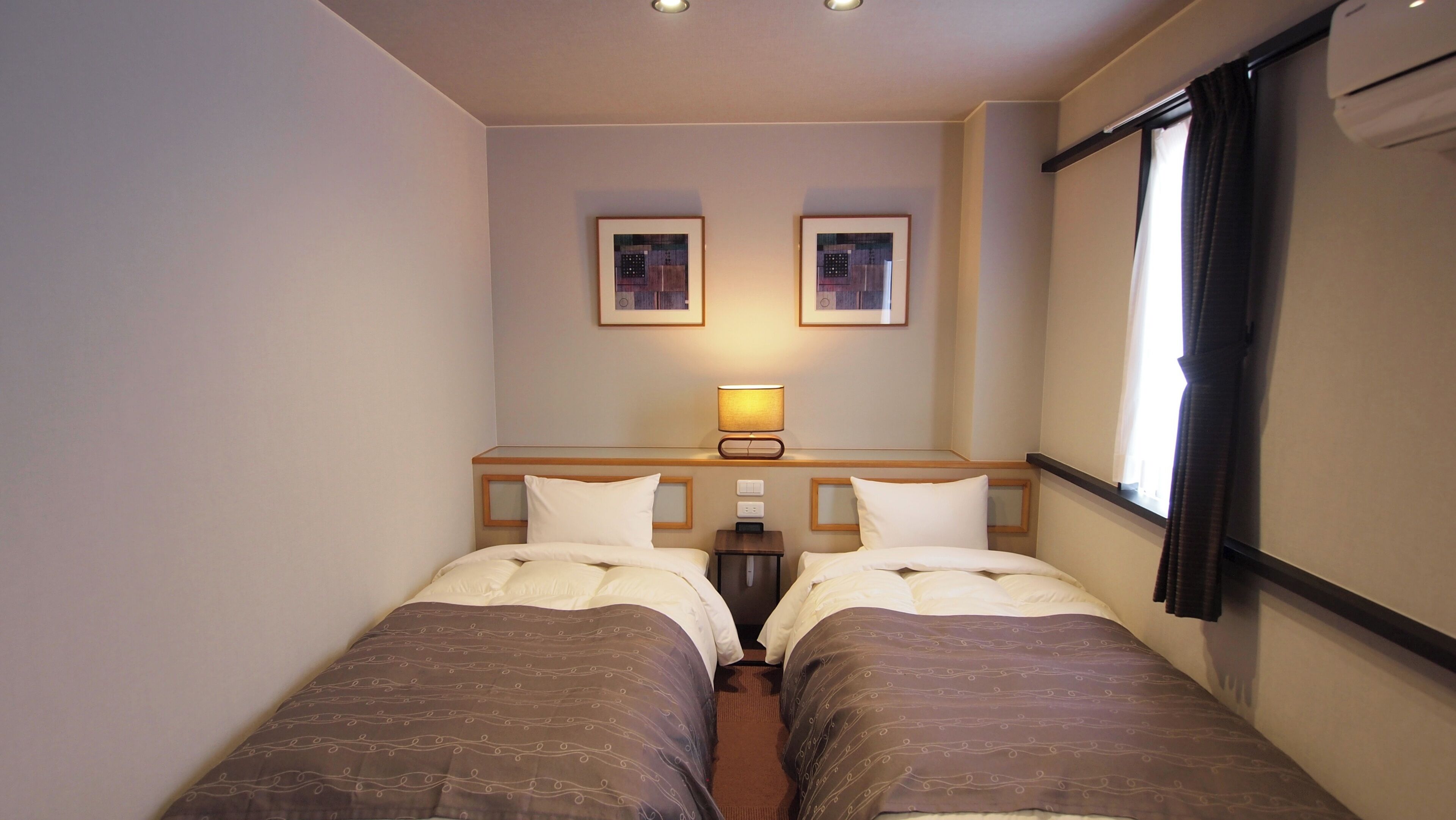 Habitación de hotel con dos camas, una mesita de noche, una lámpara y dos cuadros en la pared.