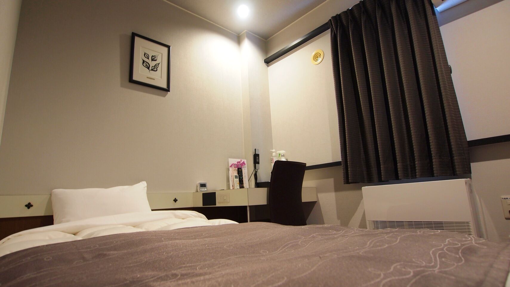 Habitación de hotel con cama, escritorio, silla, espejo y ventana con cortinas.