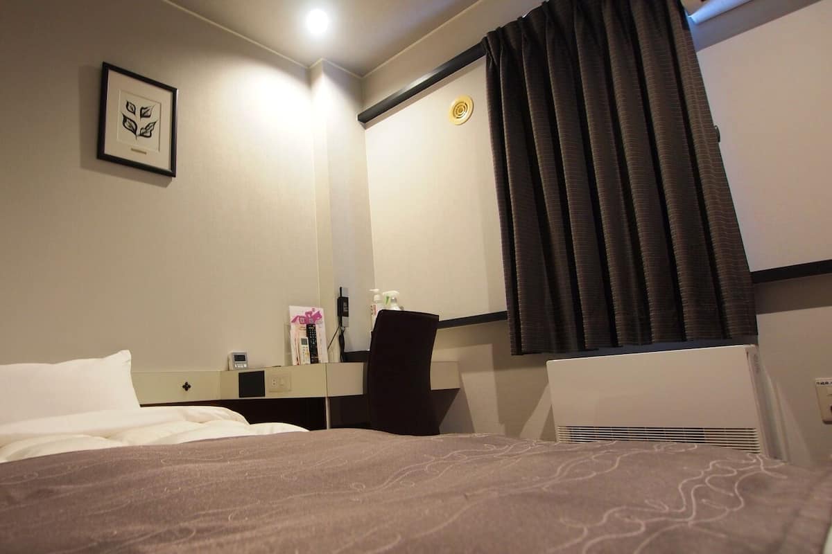 Habitación de hotel con cama, escritorio, silla, espejo y ventana con cortinas.