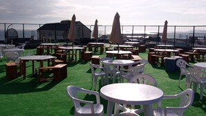 Outdoor tables and chairs on artificial grass, with umbrellas and a building in the background.