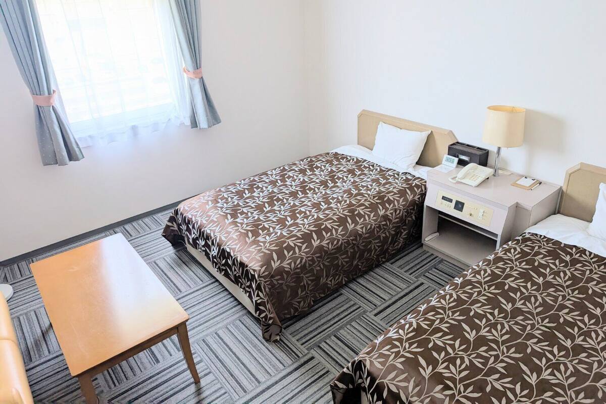 A hotel room with a bed, bedside table, lamp, and a small desk with a telephone.
