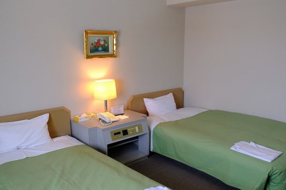Una habitación de hotel con dos camas, una mesita de noche con lámpara, teléfono y un cuadro en la pared.