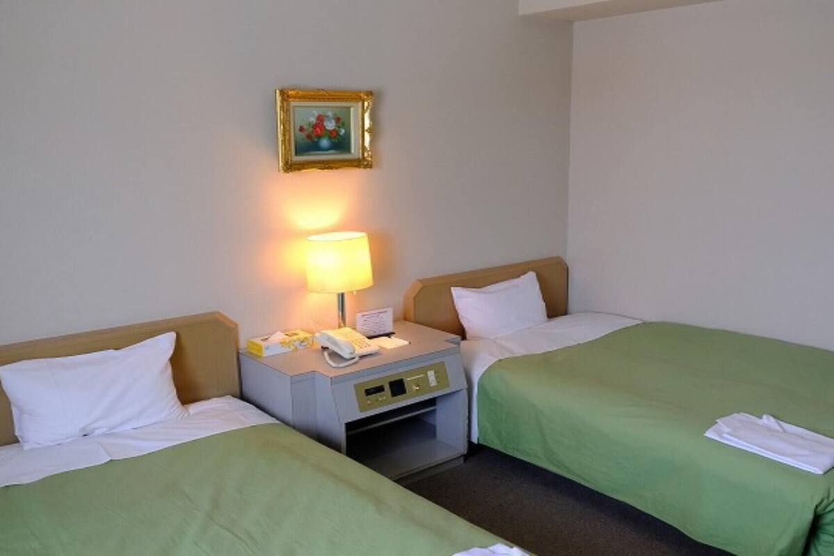 A hotel room with two beds, a nightstand with a lamp, a telephone, and a framed picture on the wall.