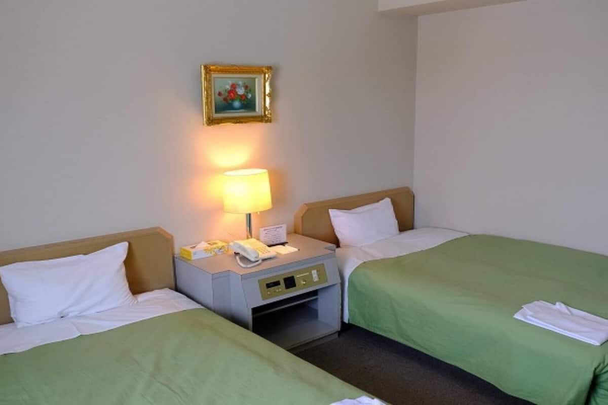 Una habitación de hotel con dos camas, una mesita de noche con lámpara, teléfono y un cuadro en la pared.