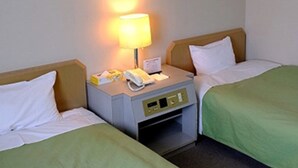 A hotel room with two single beds, a bedside table with a lamp, a telephone, and a small storage drawer.