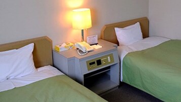 Habitación de hotel con dos camas individuales, una mesita de noche con lámpara, teléfono y un pequeño cajón.