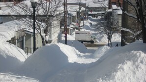 Une rue enneigée avec un camion de la société Nippon Express garé sur le bord.
