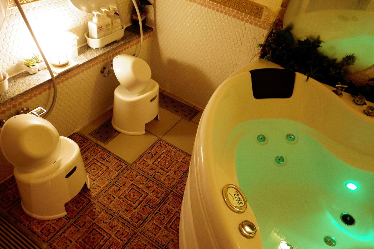 A bathroom with two toilets, a bathtub with a control panel, and a shower area.