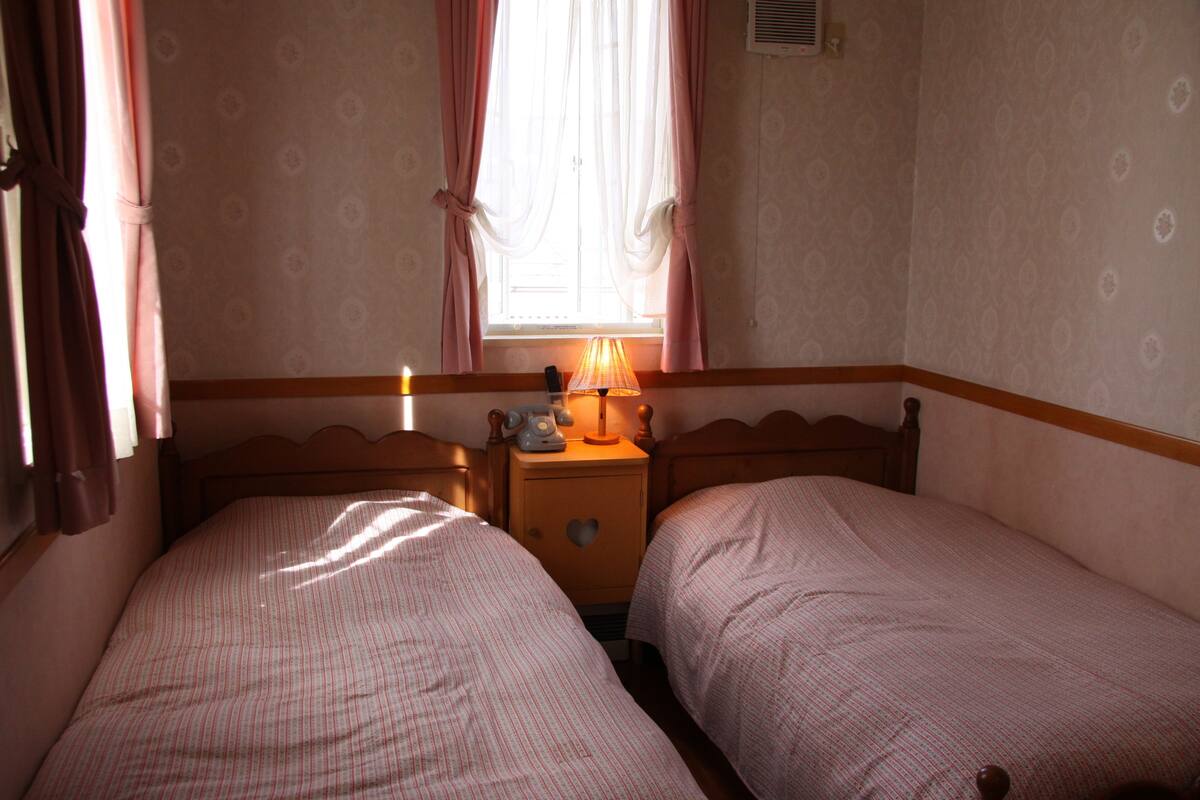 A bedroom with two beds, a nightstand with a lamp, and a window with curtains.