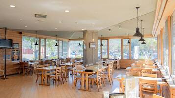 Un restaurante espacioso con mesas y sillas de madera, ventanas amplias e iluminación colgante.