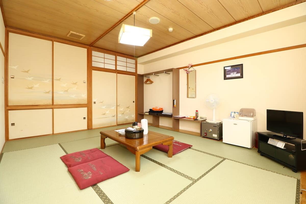 A traditional Japanese room with tatami flooring, a wooden table, a television, and a small refrigerator.