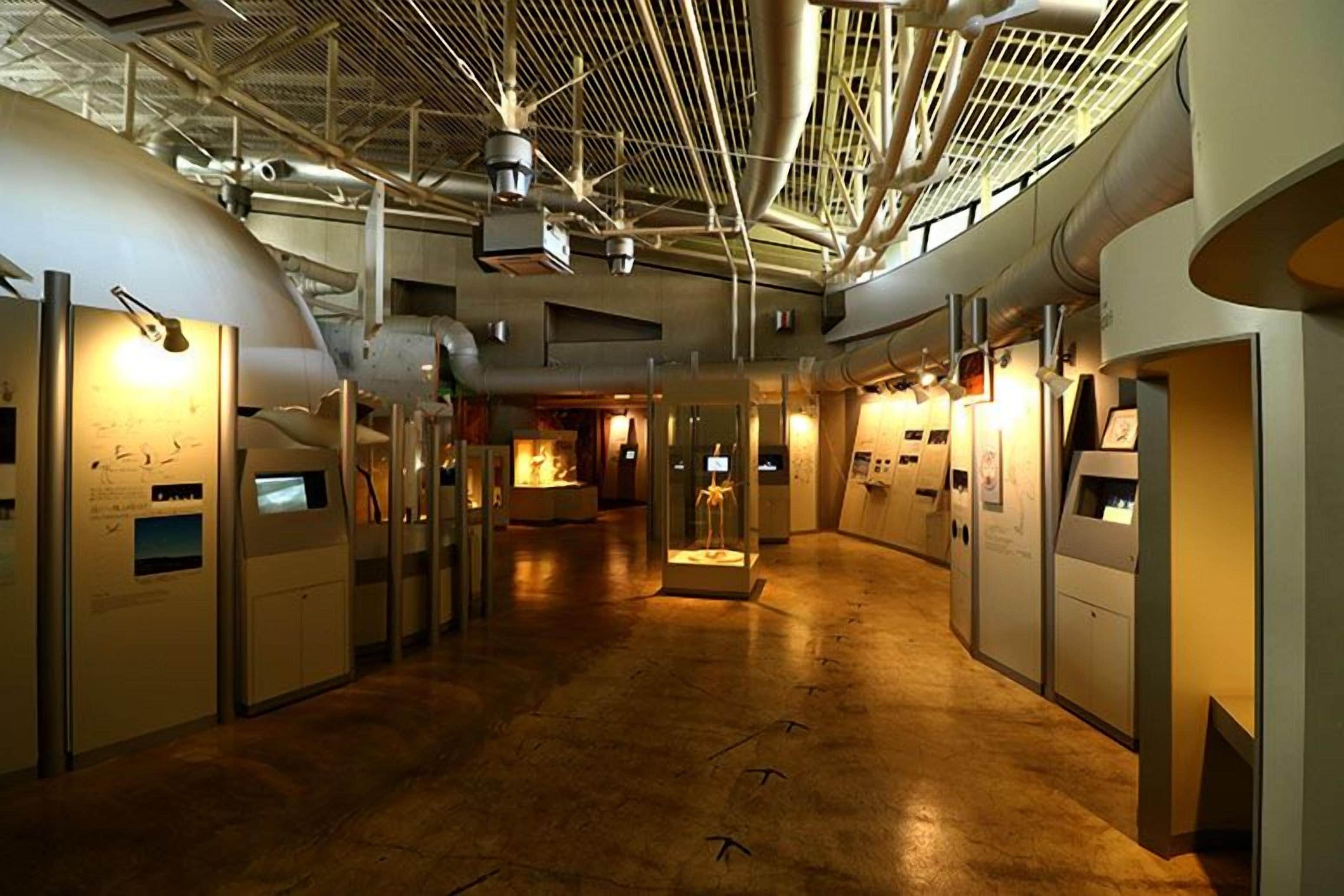 Ein Korridor mit industriellem Lichtdesign, Lüftungsrohren und einem zentralen Ausstellungsbereich.