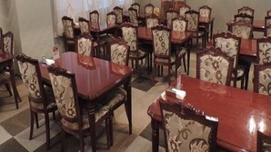 Un comedor con varias mesas y sillas, una araña y un cuadro de un paisaje urbano en la pared.