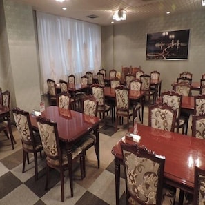 A dining area with multiple tables and chairs, a chandelier, and a cityscape painting on the wall.