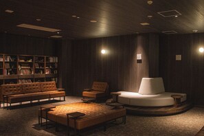 A dimly lit room with a sofa, armchairs, a white armchair, and a bookshelf. - Rembrandt Resort Shiretoko (Shari)