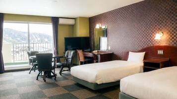 A hotel room with two beds, a desk with a chair, a TV, and a large window.