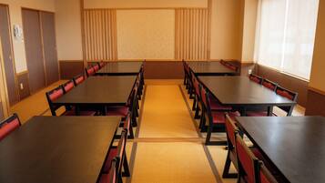 A conference room with multiple tables and chairs, a carpeted floor, and a large window on one side.