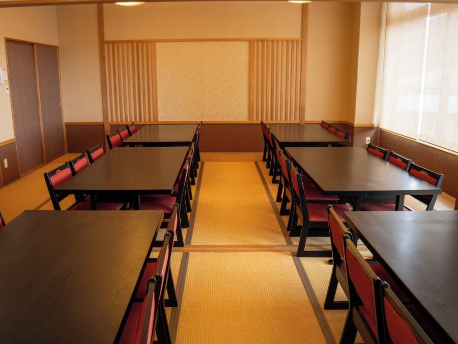 A conference room with multiple tables and chairs, a carpeted floor, and a large window on one side.